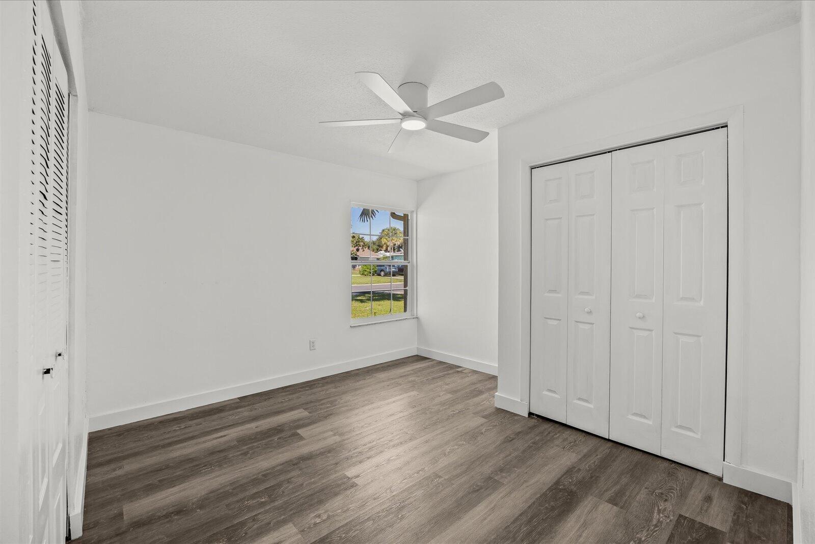 Interior room featuring wood-finish flooring, a ceiling fan with integrated lighting, a single window, and a white bifold closet door