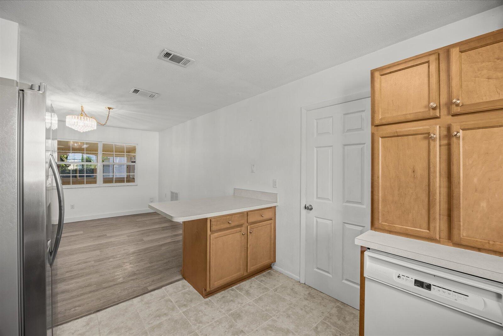 Kitchen featuring light wood-finish cabinetry, a peninsula with a solid-surface countertop, stainless steel refrigerator, white dishwasher, and wood-finish flooring