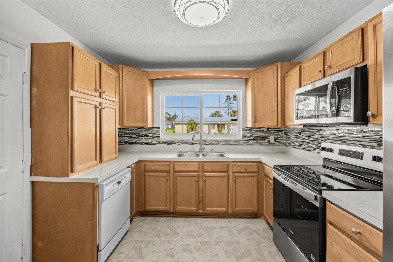 Kitchen featuring wood cabinetry, solid-surface countertops, decorative stone-style tile backsplash, stainless steel microwave, and dual-basin sink with arched-neck faucet