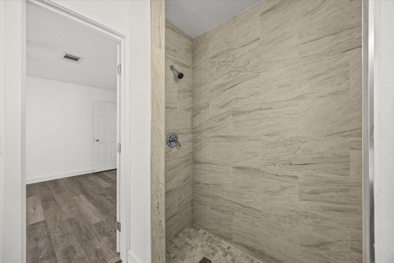 Walk-in shower featuring floor-to-ceiling stone-patterned tile, stone-tiled flooring, and a metallic shower fixture