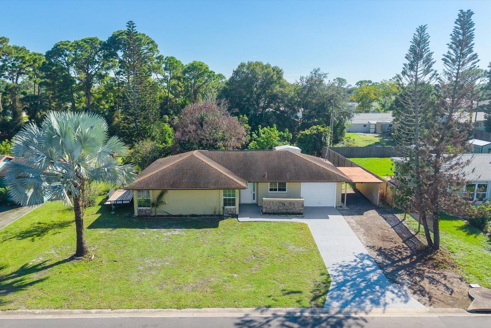 Single-story exterior featuring a hip roof, stone veneer accents, an attached carport, and a concrete driveway