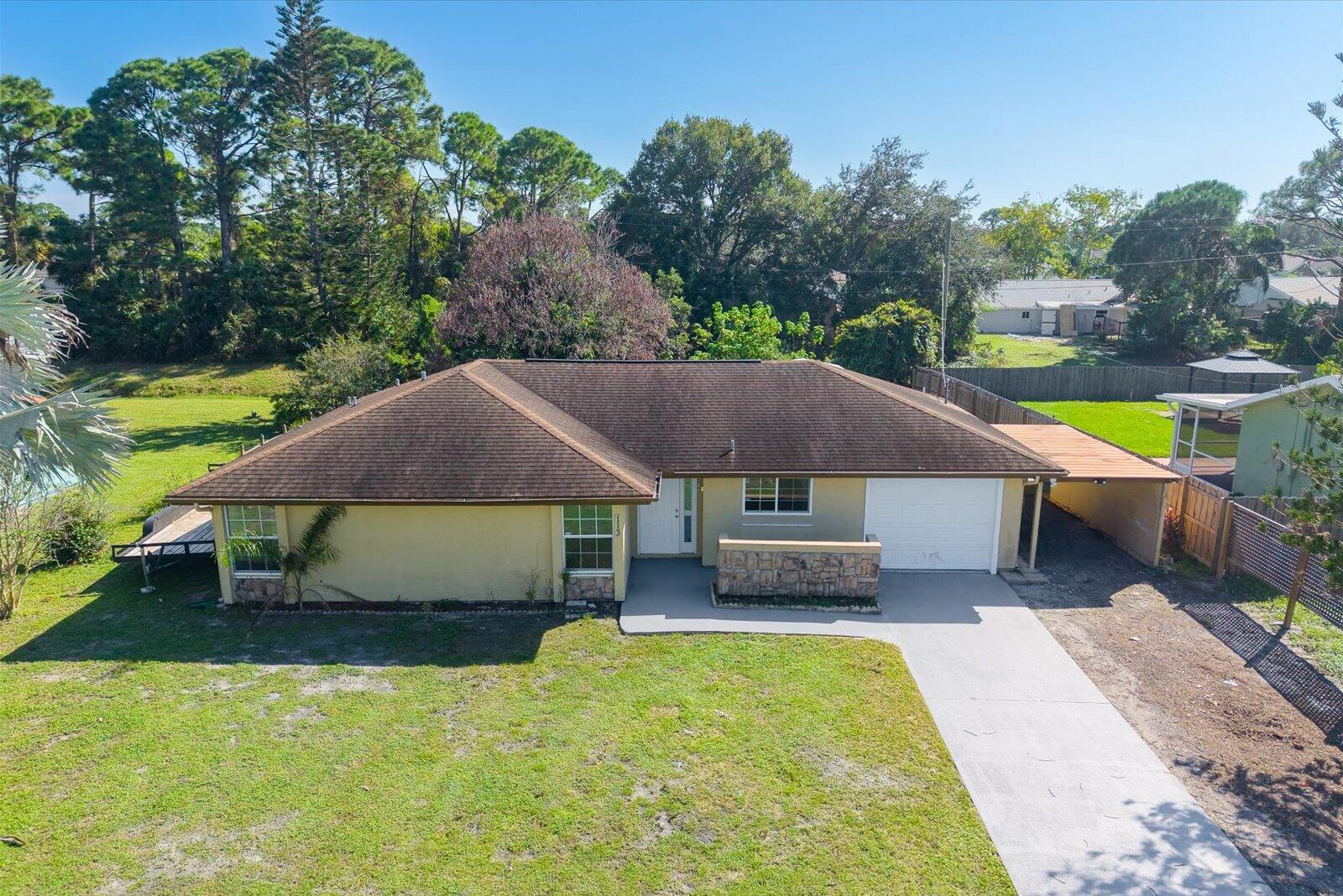 Single-story residence featuring a hipped roof, stone-veneer exterior accents, attached garage, and a covered side carport