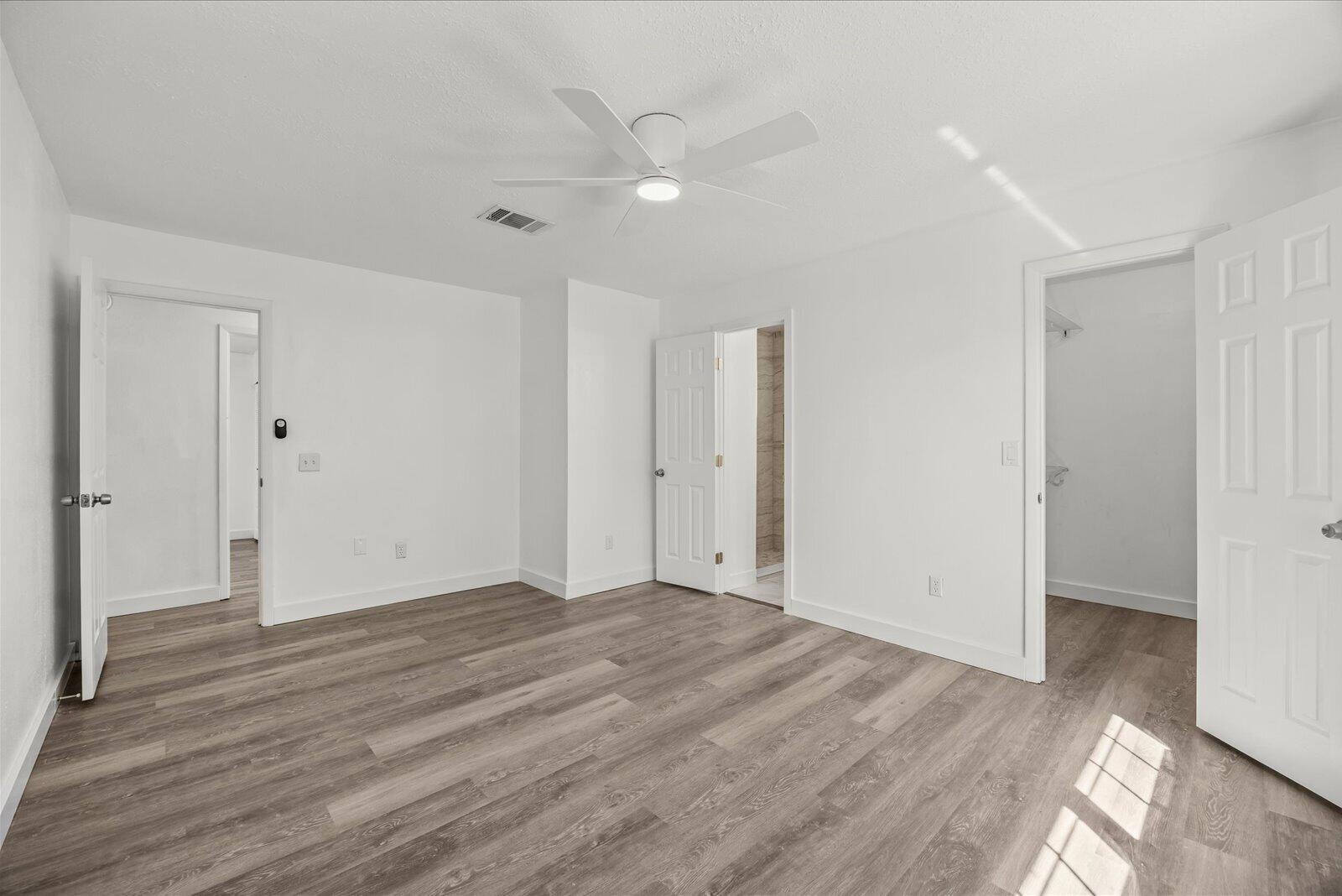 Wood-finish flooring, white walls, and a ceiling fan with integrated lighting