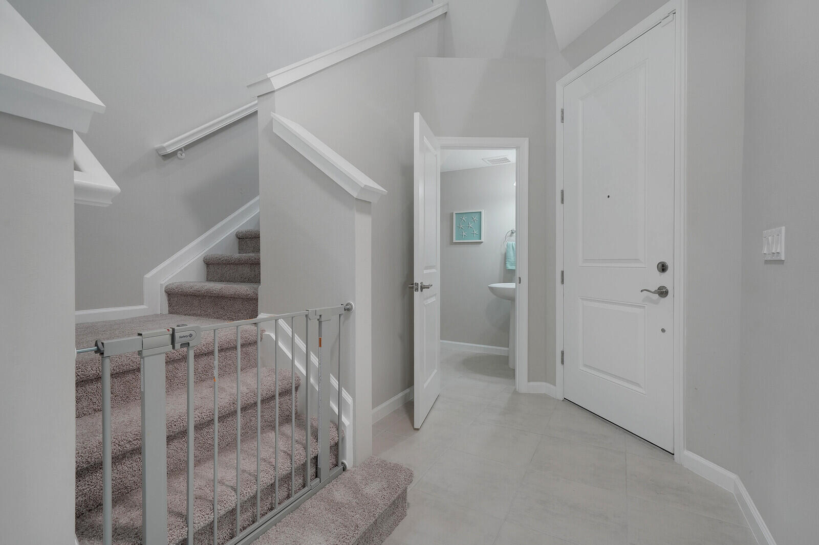 Foyer featuring tile flooring, a paneled front door with metallic hardware, and a carpeted staircase with a white handrail