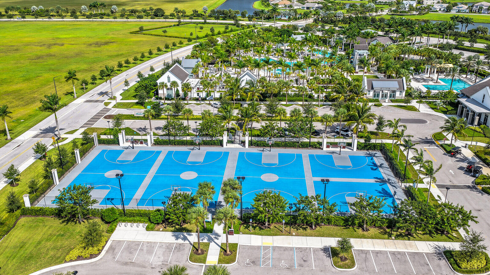 Outdoor athletic facility featuring multiple basketball courts with blue surfacing, perimeter fencing, and integrated lighting fixtures