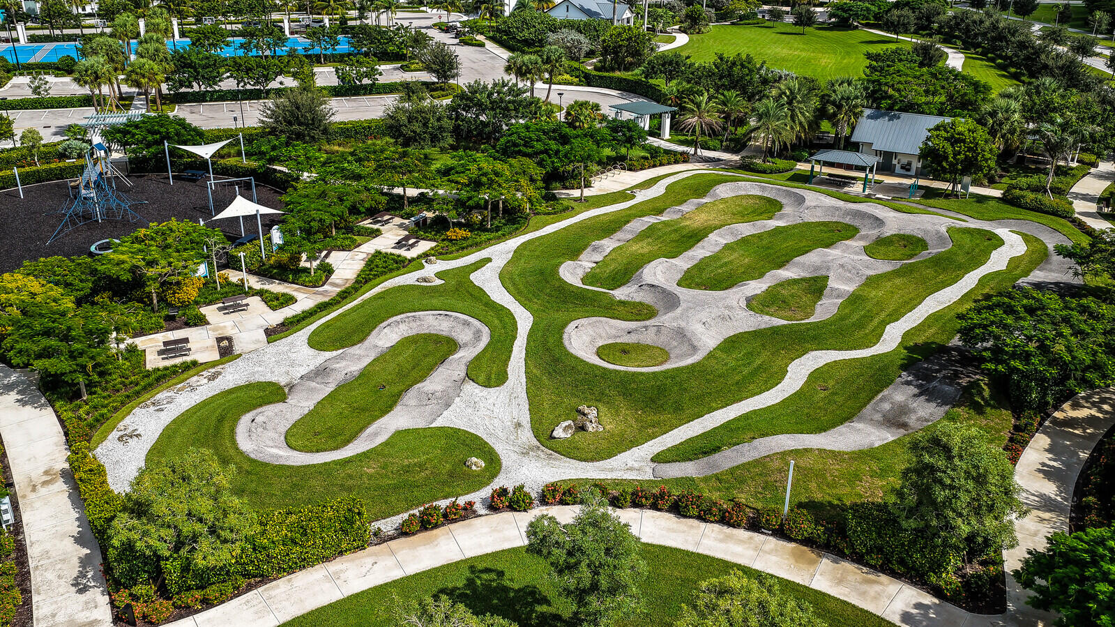 Community recreational area featuring a paved pump track, manicured turf, landscaped green space, and integrated pedestrian pathways