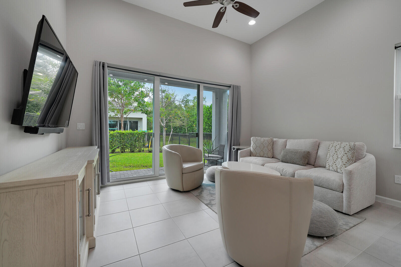 Living area featuring high ceilings, large-format tile flooring, a ceiling fan, and sliding glass doors with access to a paved patio and backyard