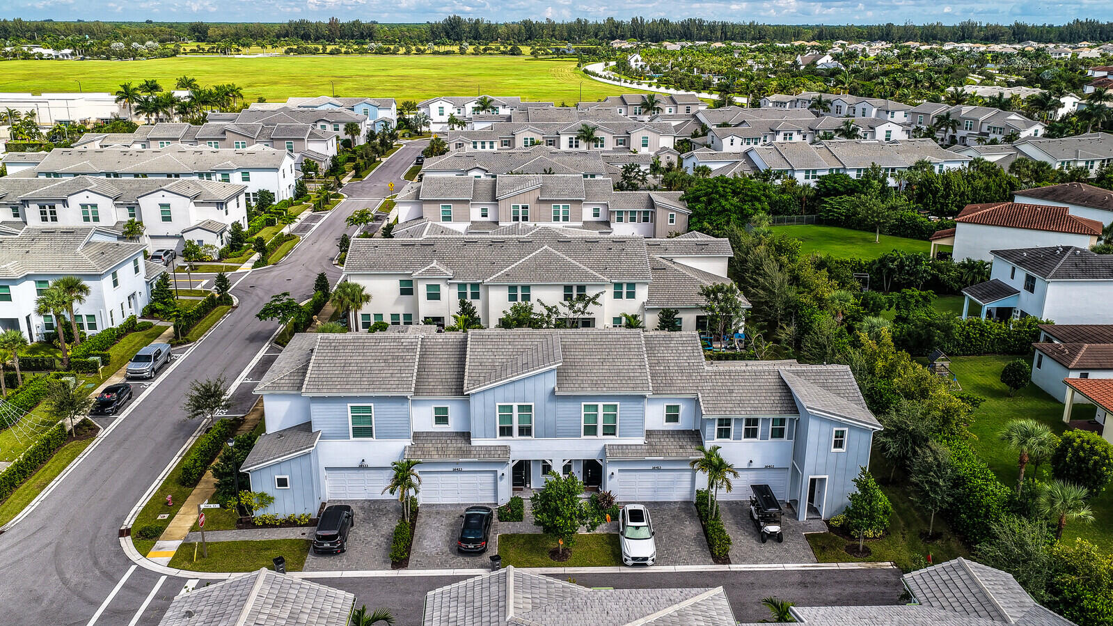 Multi-unit residential complex featuring gabled rooflines, light-toned horizontal siding, paved driveways, and integrated garage doors