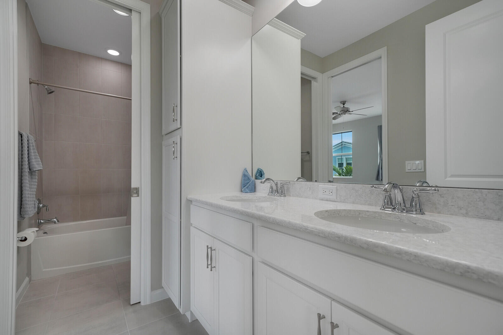 Double vanity featuring white cabinetry, stone-finish countertops, polished chrome fixtures, and a floor-to-ceiling storage cabinet, paired with a full-height tiled shower and tub combination