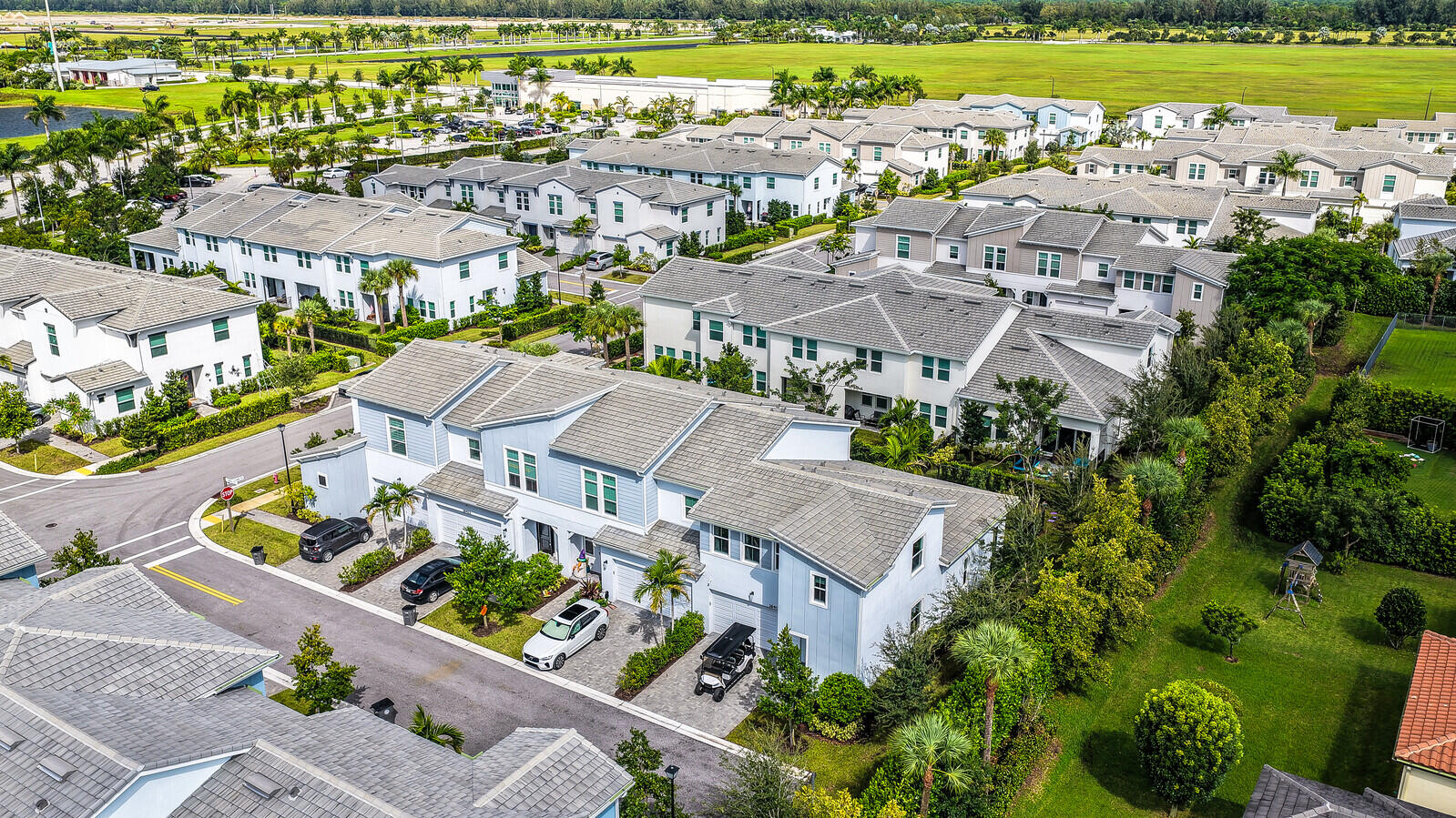 Aerial perspective of multi-story residences featuring light-toned siding, grey shingled roofs, integrated garages, and paver driveways