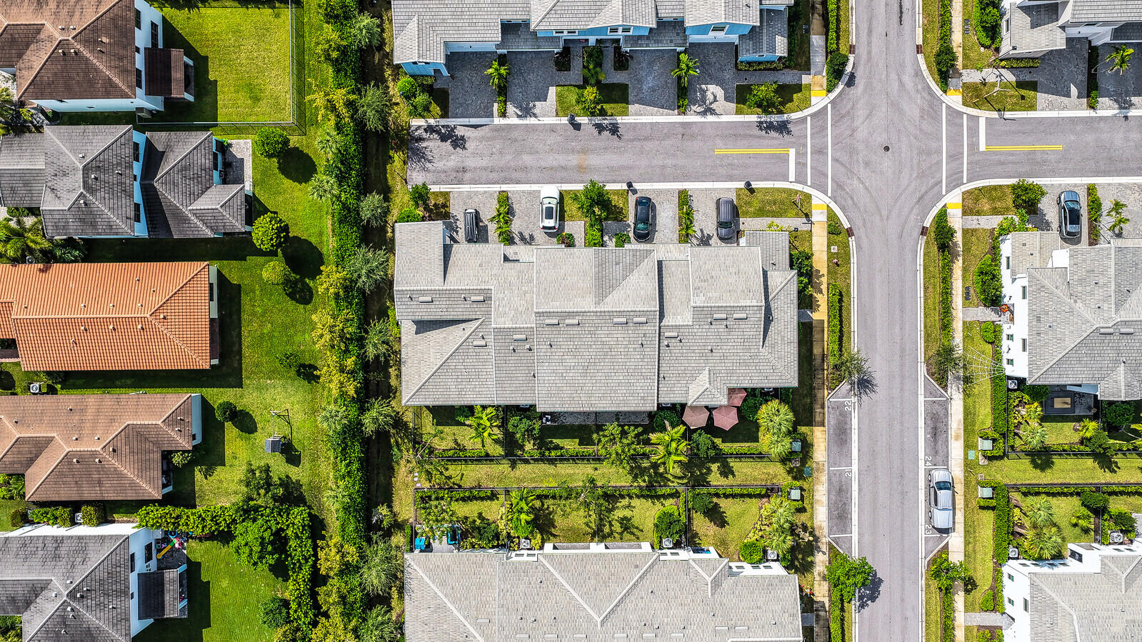 Aerial perspective of a multi-unit residential property featuring a shingle roof, concrete-paved motor court, and landscaped perimeter hedges