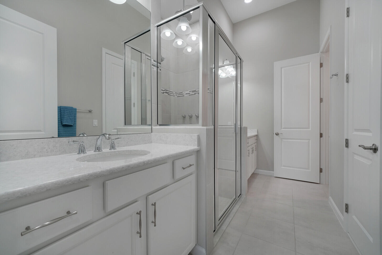 Large Ensuite Primary Bathroom with Dual Sinks, Walk in Closet, Linen Closet, White cabinetry with brushed nickel hardware, Quartz countertops, undermount sink, and glass-enclosed shower with tile surround.