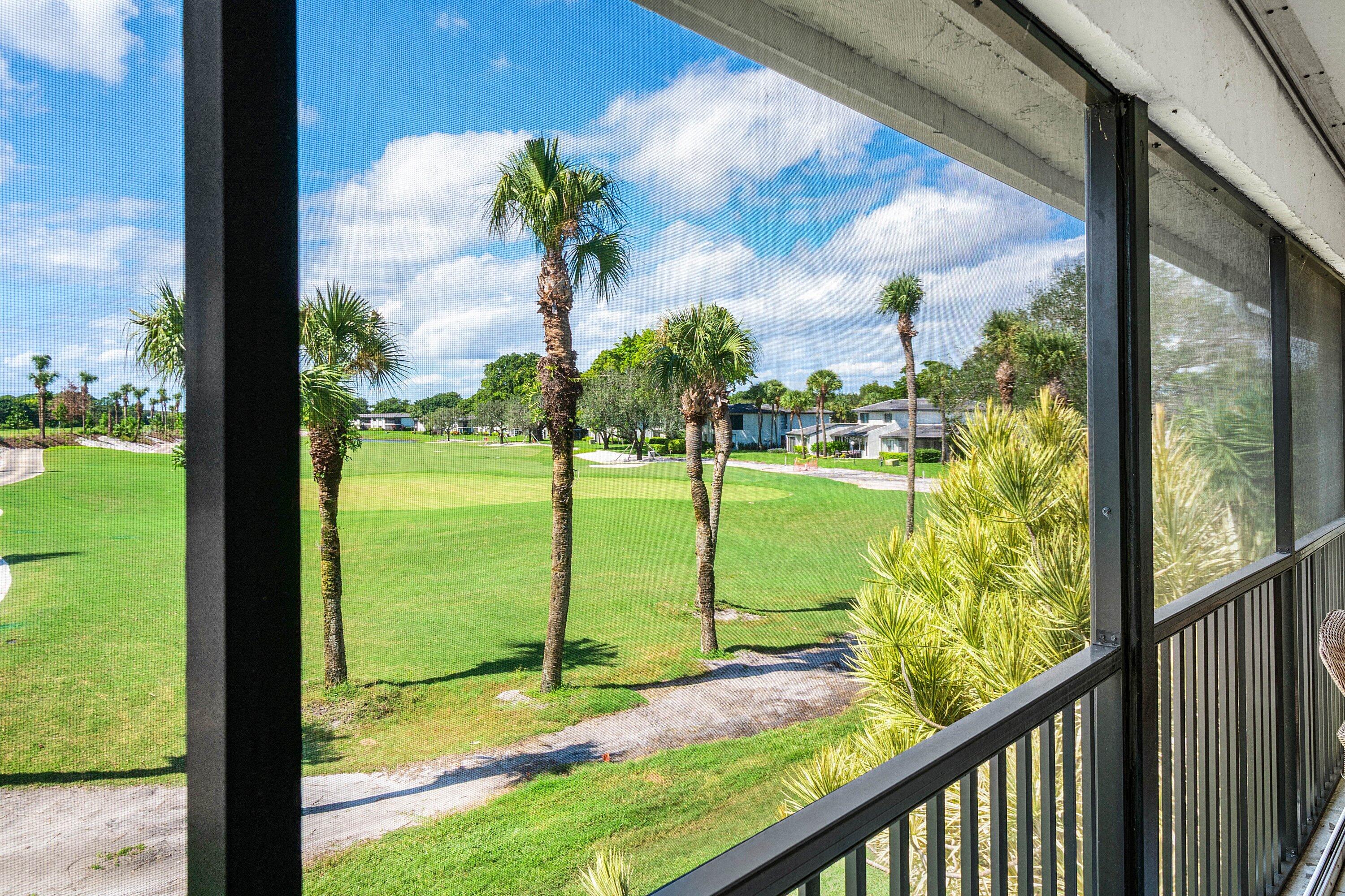 Screened-in balcony featuring a metal railing and expansive golf course landscape with mature palm trees