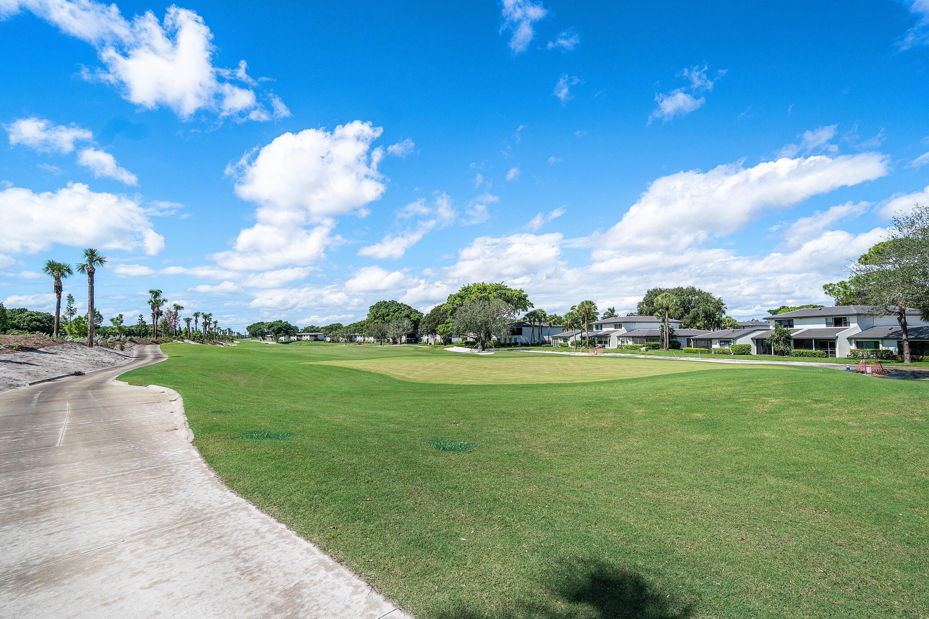 Expansive golf course grounds featuring a concrete cart path, manicured turf, mature trees, and landscaping