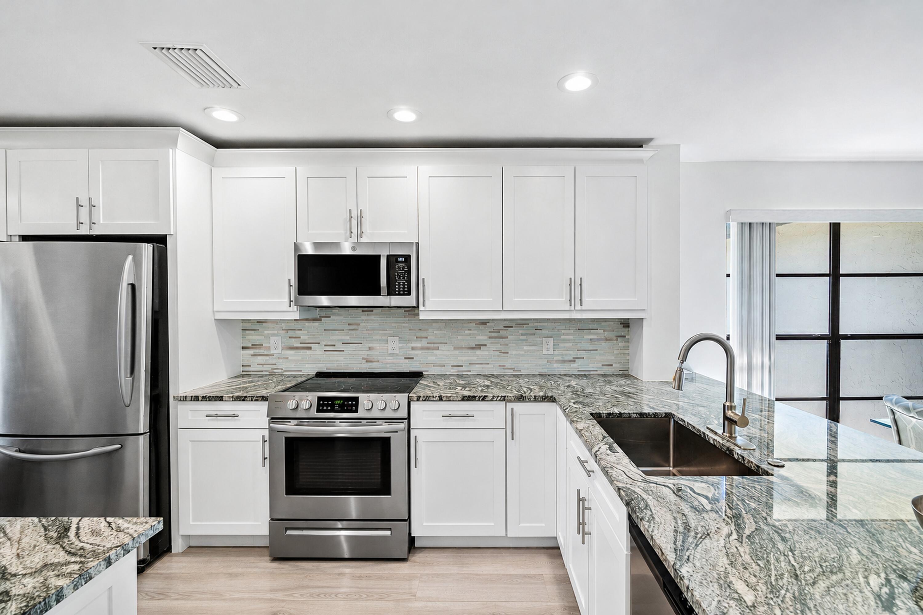 Kitchen featuring white shaker-style cabinetry, patterned stone countertops, stainless steel appliances, a multi-tonal linear tile backsplash, and an undermount stainless steel sink with a high-arc faucet Kitchen featuring white shaker-style cabinetry, patterned stone countertops, stainless steel appliances, a multi-tonal linear tile backsplash, and an undermount stainless steel sink with a high-arc faucet