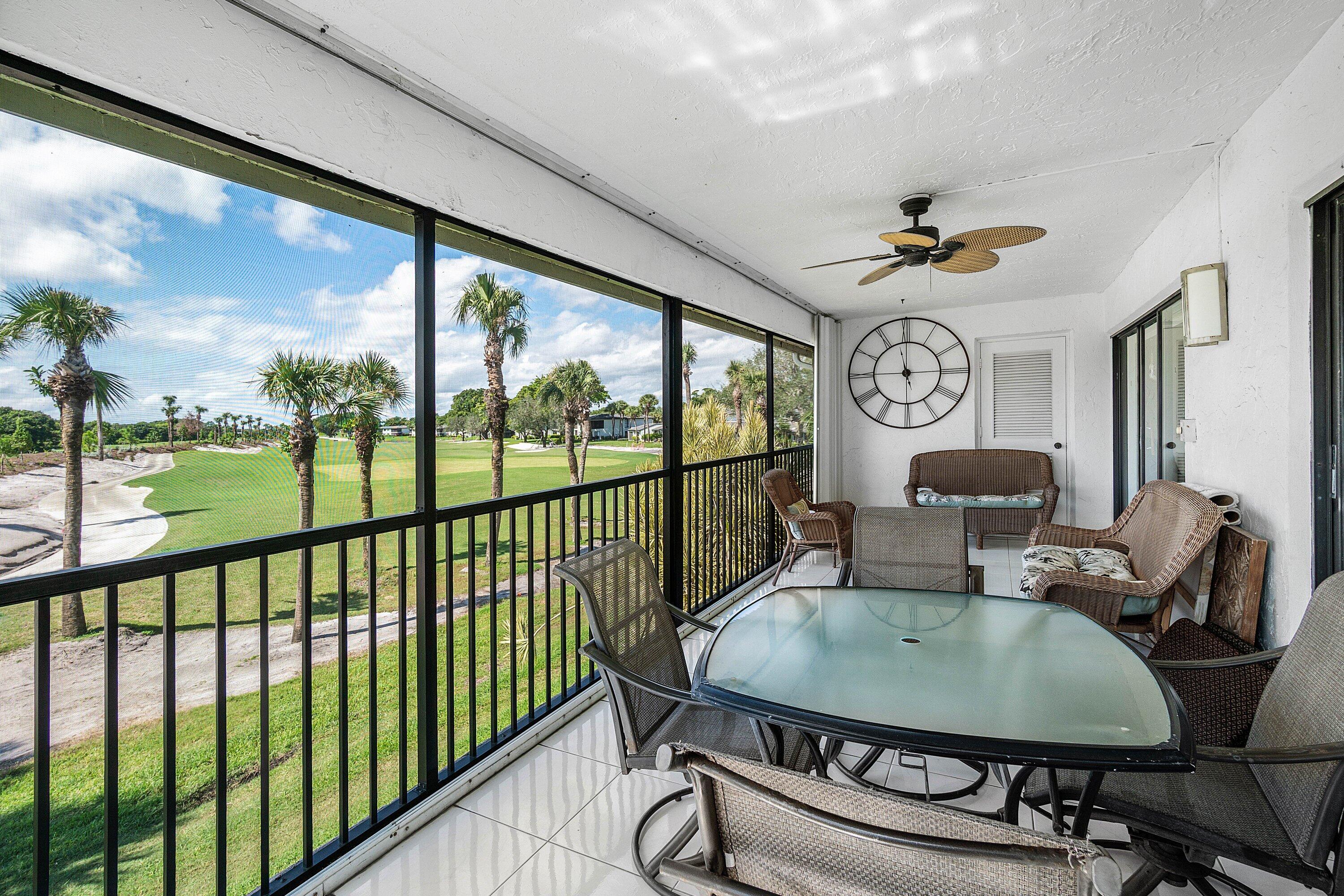 Screened-in balcony with tile flooring, black metal railing, and overhead ceiling fan, featuring an expansive outdoor perspective