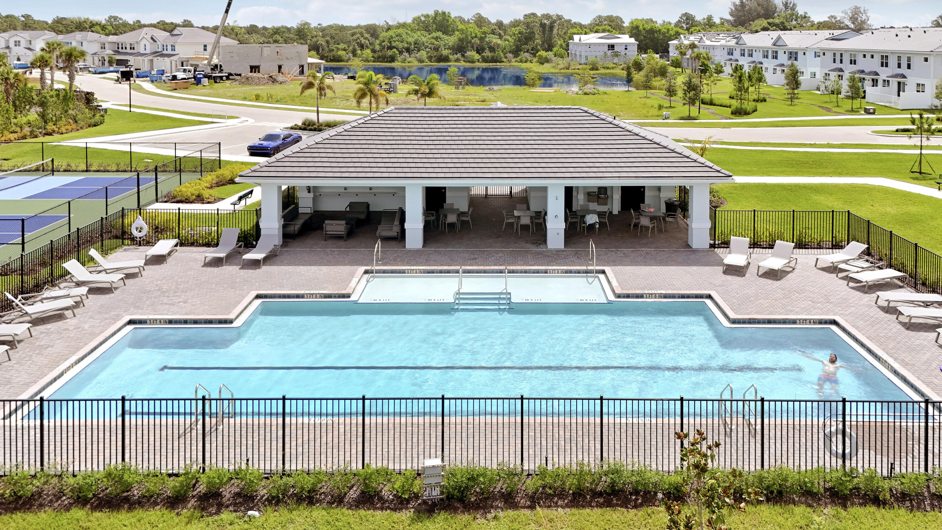 Community swimming pool with paver decking, covered pavilion, metal fencing, and pickleball court.