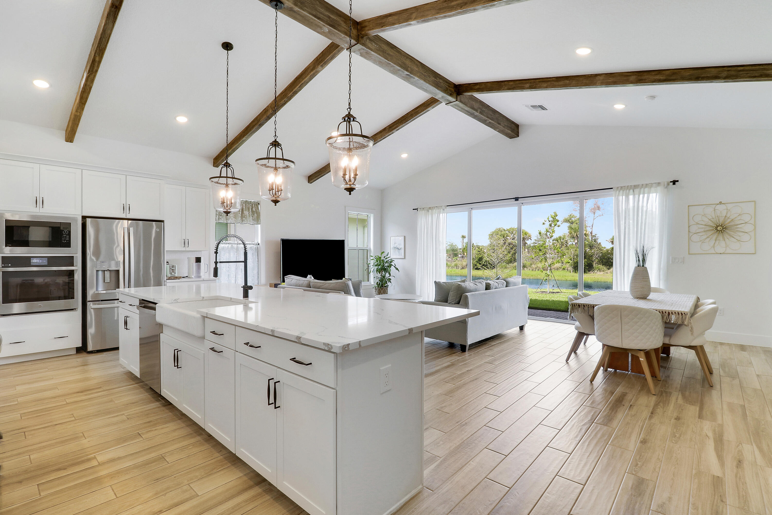 Kitchen featuring vaulted ceilings imitating wood beams, an expansive center island with a farmhouse-style sink, quartz countertops, pendant lighting, and wood-finish tile flooring
