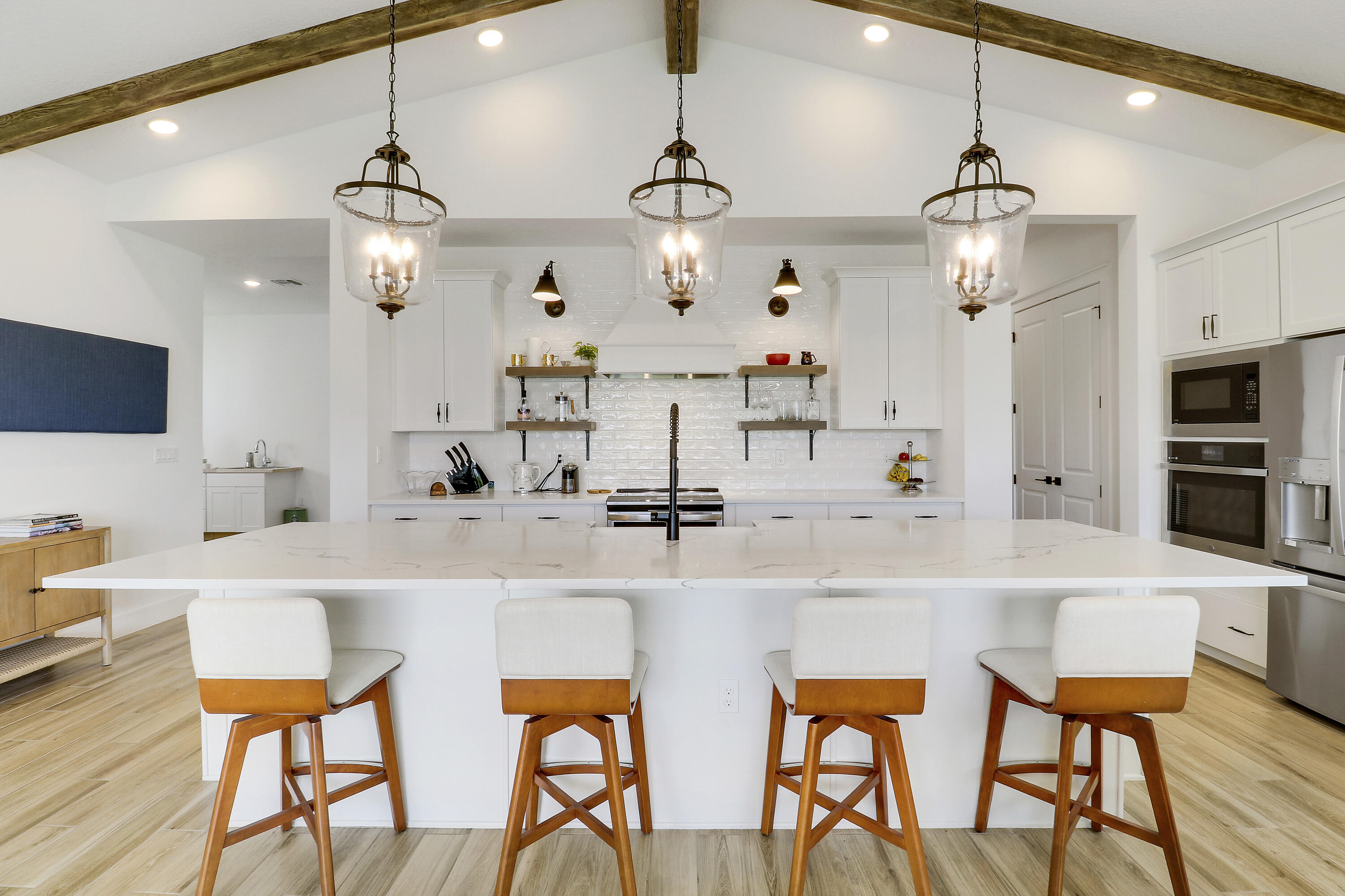Kitchen featuring a central island with a stone-finish countertop, vaulted ceiling with exposed wood-finish like beams, white cabinetry, lantern-style pendant lighting, and subway tile backsplash