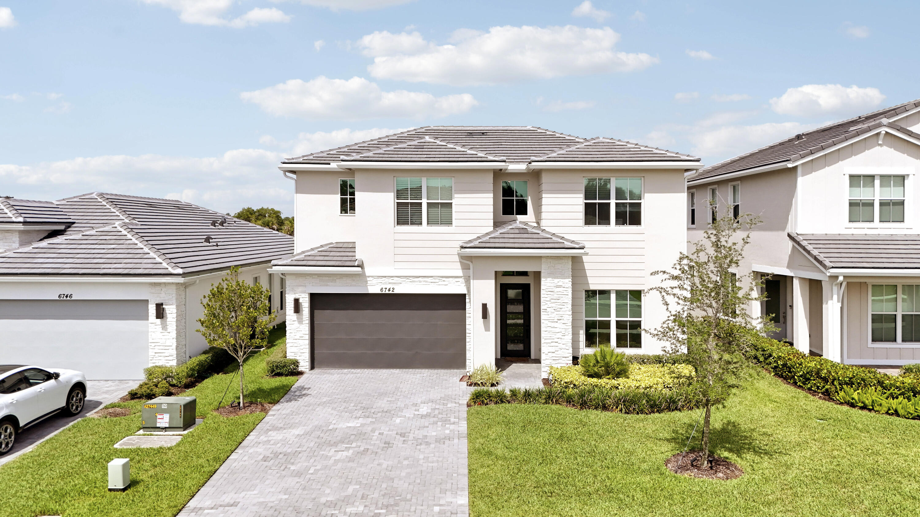 Two-story exterior featuring stone veneer accents, horizontal siding, a tiled roof, and a paved driveway leading to a multi-car garage