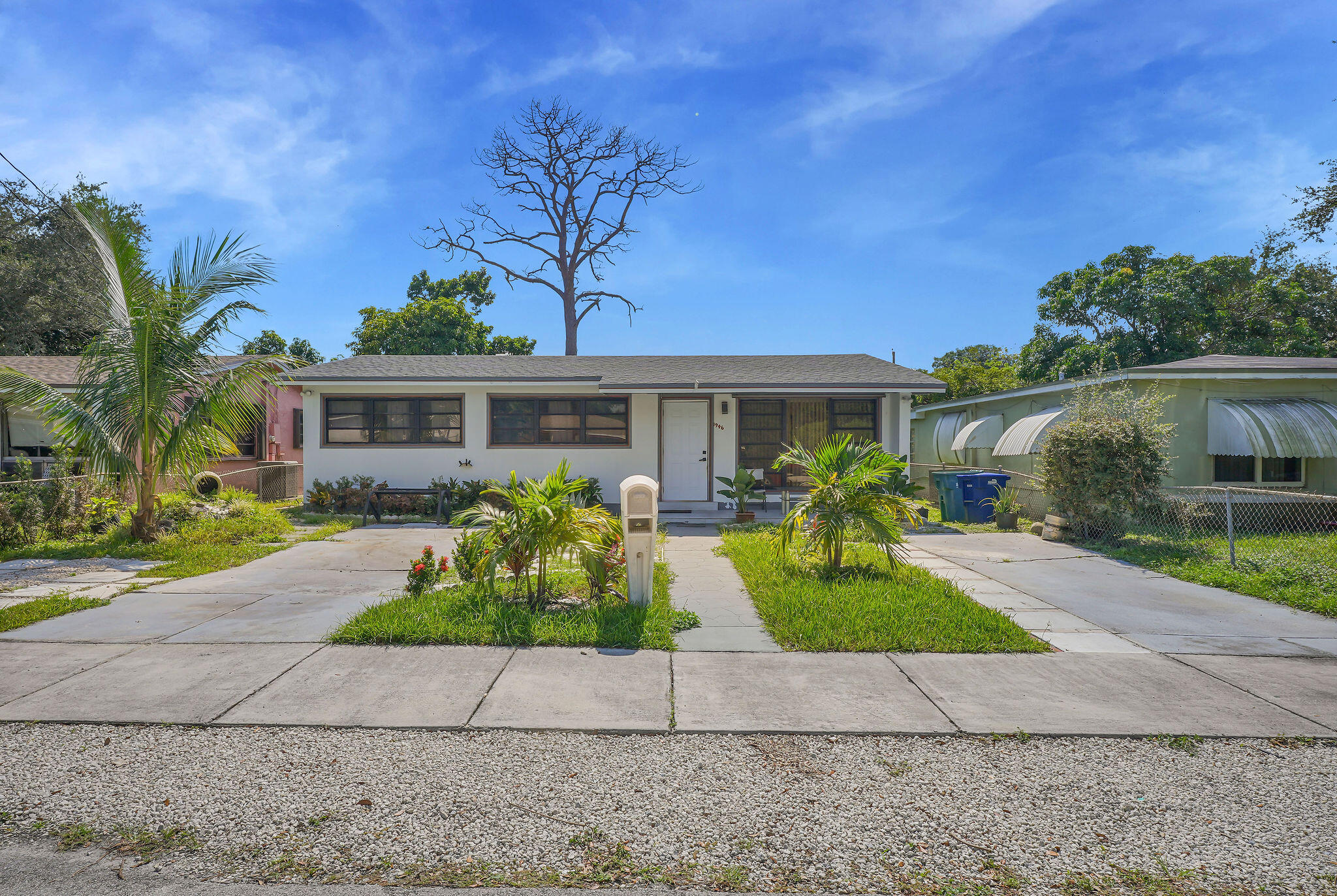 Single-story exterior featuring a light-colored facade, dual concrete driveways, and established tropical landscaping