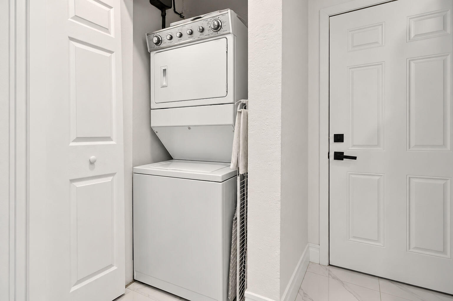 Laundry area featuring a stacked washer and dryer unit, four-panel interior doors, and tile flooring