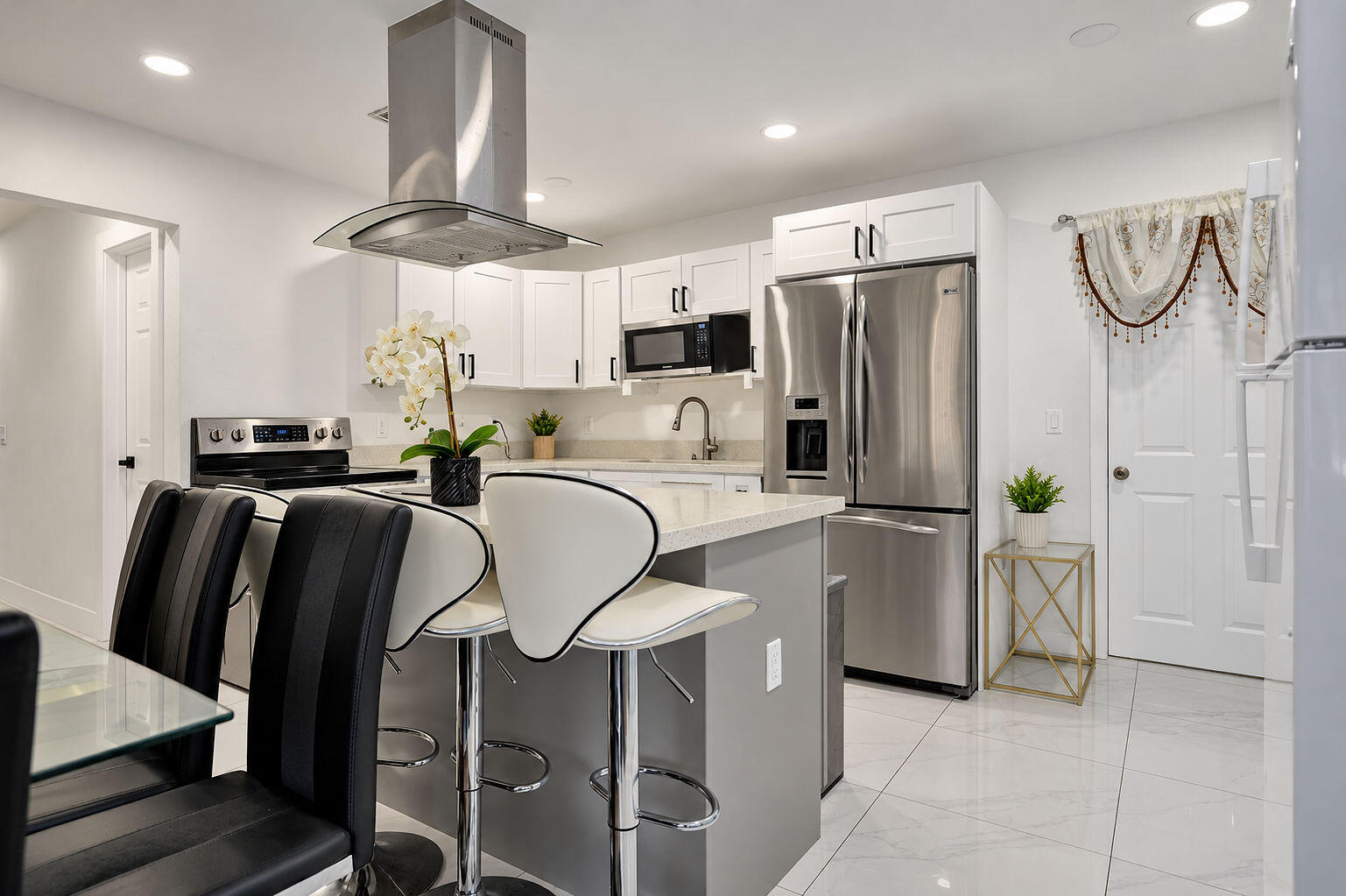 Kitchen featuring white shaker-style cabinetry, quartz countertops, stainless steel appliances, a stainless steel range hood, and tile flooring