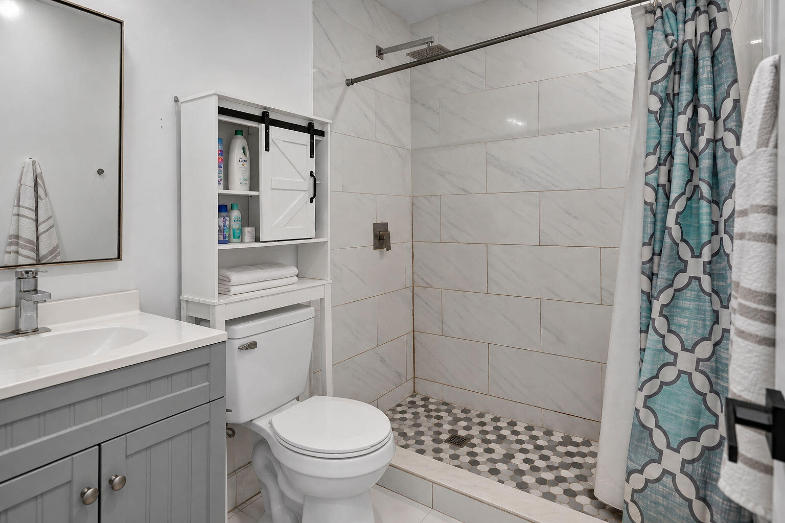 Grey shaker-style vanity with a solid surface countertop, rectangular under-mount sink, white subway-style shower wall tile, and geometric patterned shower floor tile