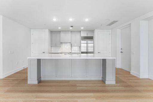 Kitchen featuring a large central island with solid-surface countertops, custom shaker-style cabinetry, stainless steel built-in refrigerator, recessed lighting, and wood-finish flooring