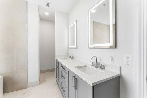 Dual-sink vanity featuring grey cabinetry, white countertops, rectangular undermount sinks, chrome hardware, and LED-integrated mirrors