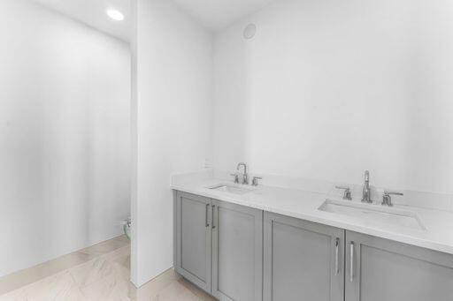 Double vanity featuring gray shaker-style cabinetry, solid-surface countertops, undermount sinks, and polished chrome widespread faucets