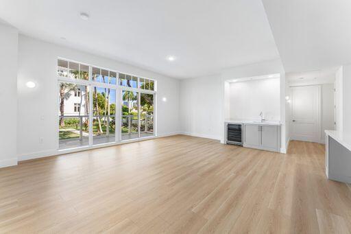 Open-concept room featuring wood-finish flooring, a wet bar with under-counter cabinetry and sink, built-in beverage refrigerator, and expansive floor-to-ceiling windows