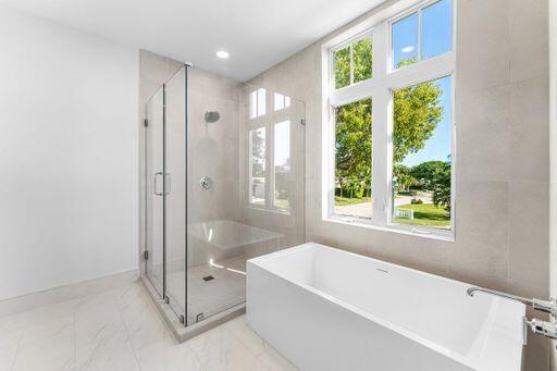 Freestanding rectangular soaking tub with polished chrome faucet, glass-enclosed shower with tiled surround, and expansive window with exterior greenery