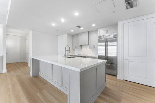 Kitchen featuring an expansive center island with a stone countertop, shaker-style cabinetry, stainless steel refrigerator, and wood-finish flooring