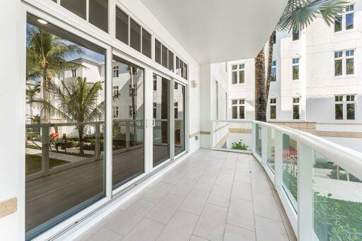 Covered balcony featuring light-toned tile flooring, glass panel railings, and full-height multi-panel sliding glass doors with transom windows