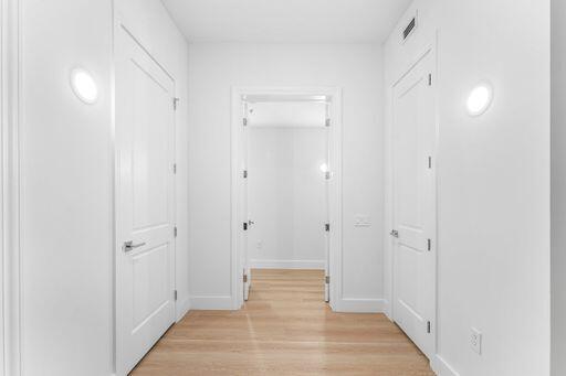 Hallway featuring wood-finish flooring, two-panel interior doors with brushed nickel hardware, and wall-mounted circular light fixtures