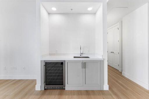 Built-in bar area featuring light-gray shaker cabinetry, a white countertop, an integrated beverage cooler, and a stainless steel sink with a high-arch faucet