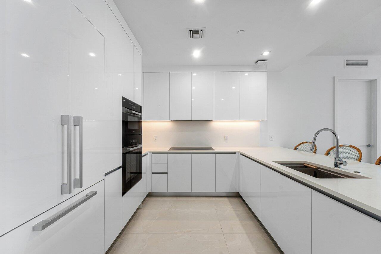 Kitchen featuring high-gloss cabinetry, stone countertops, integrated wall ovens, a cooktop, and an undermount sink with a gooseneck faucet