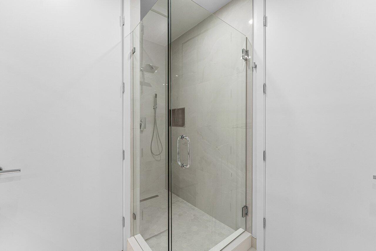 Walk-in shower featuring a glass enclosure with polished hardware, oversized wall tile, rainfall showerhead, and wall-mounted hand shower