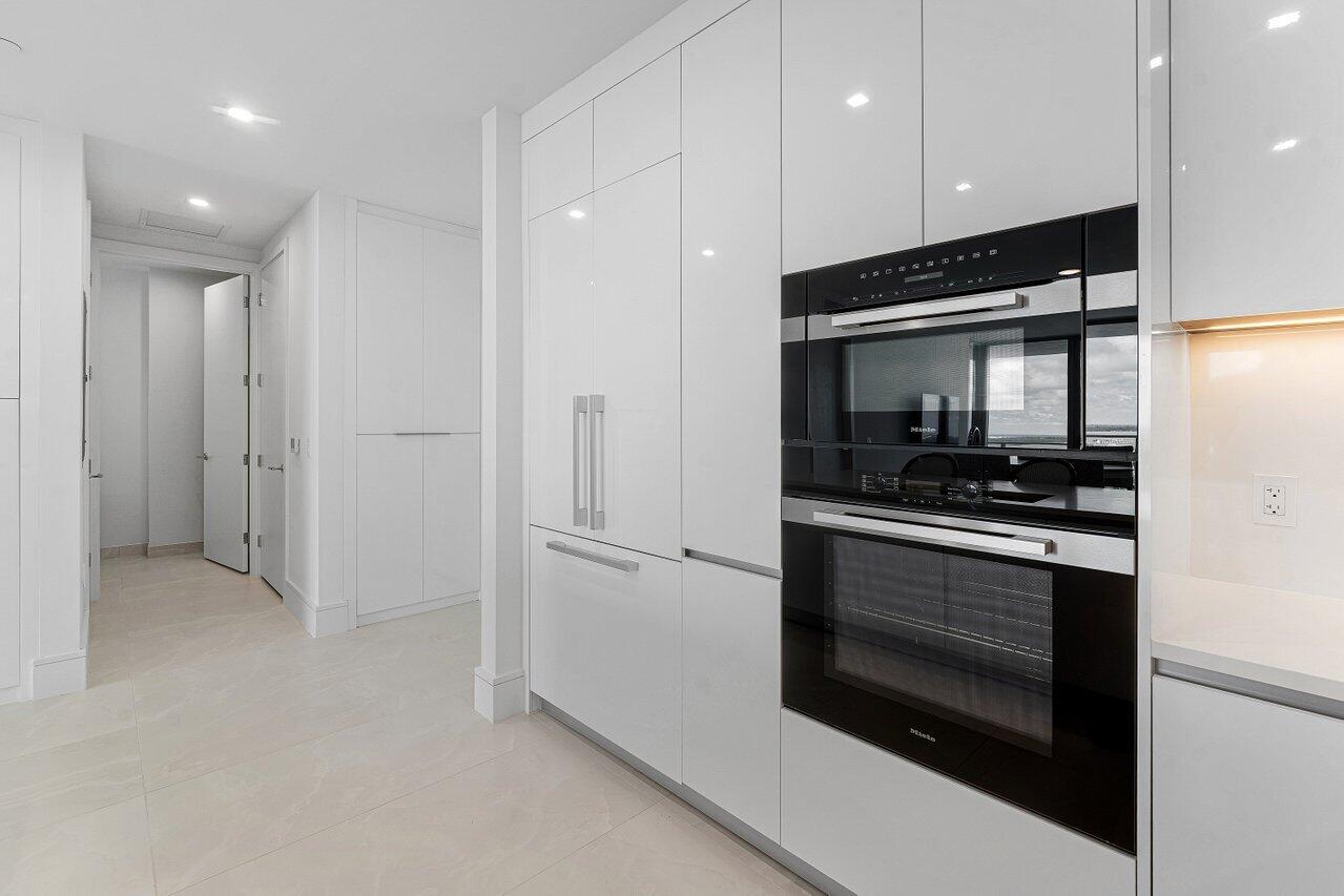 Kitchen featuring floor-to-ceiling high-gloss white cabinetry, integrated stainless steel appliances, a built-in wall oven, and light-toned tile flooring