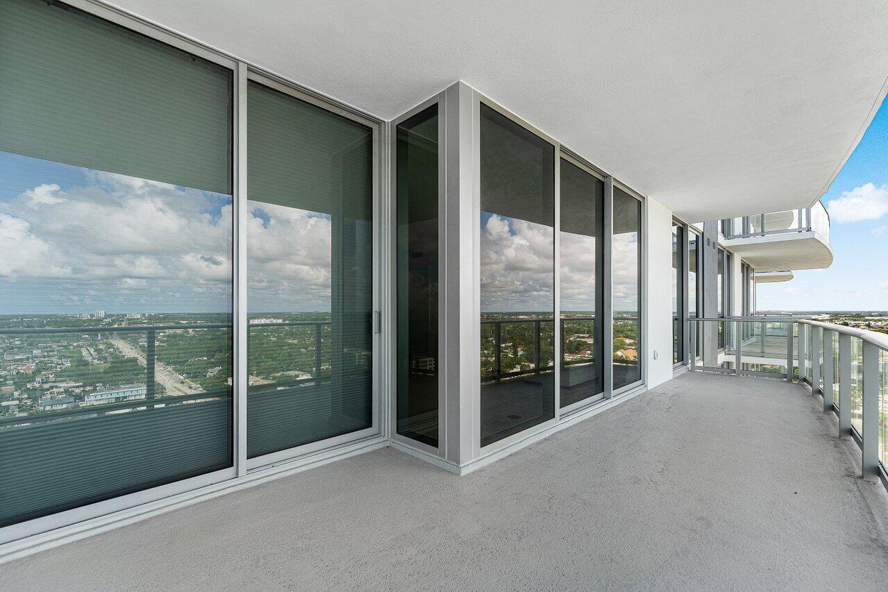 Covered wrap-around balcony featuring floor-to-ceiling glass panel walls, a concrete floor surface, and metal railing