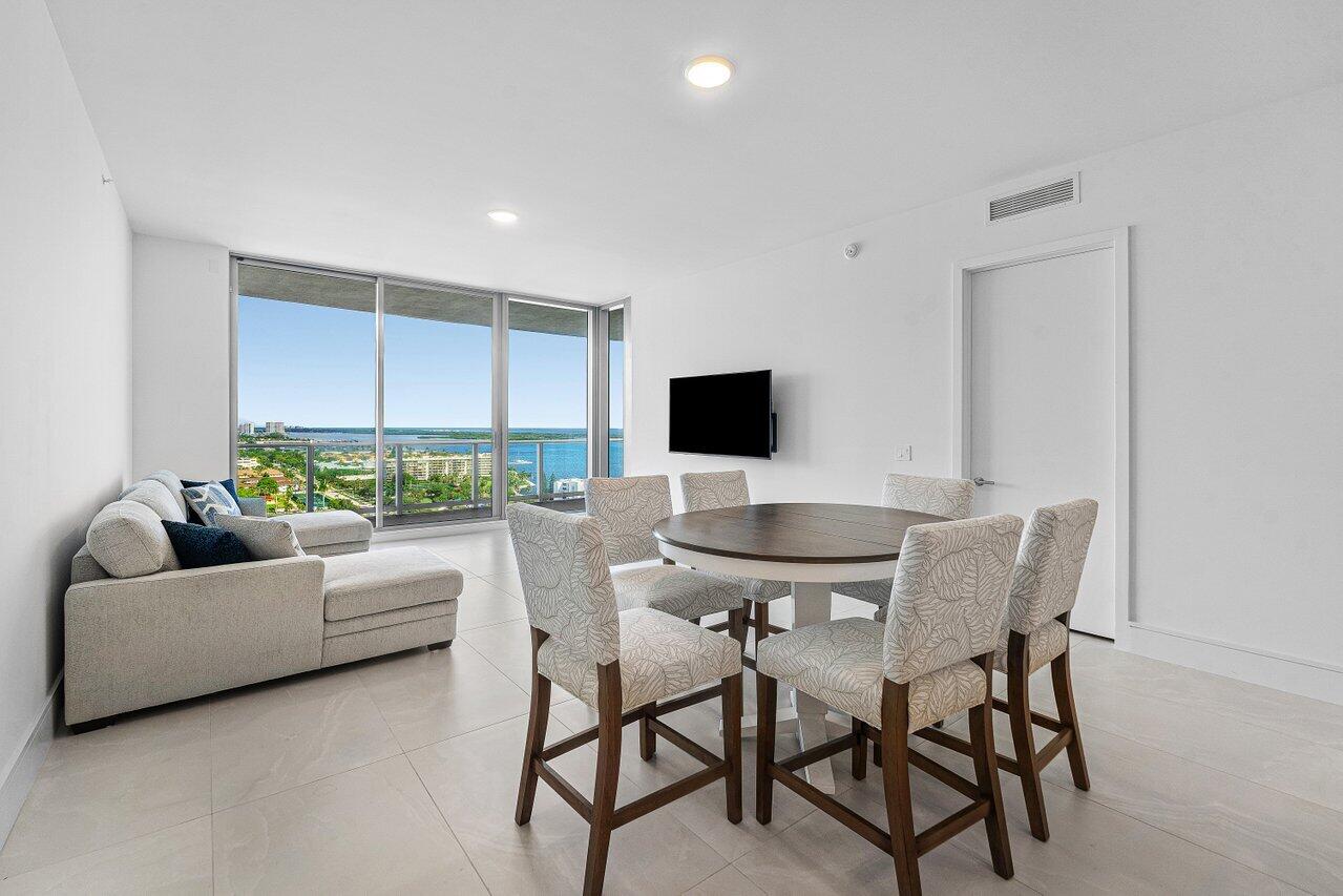 Open-concept interior featuring large-format tile flooring, recessed lighting, and floor-to-ceiling glass doors opening to a balcony with water and coastal scenery