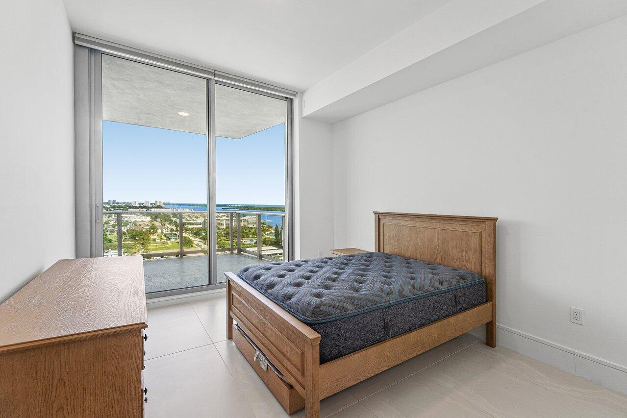 Floor-to-ceiling sliding glass doors, private balcony with metal railing, light-colored tile flooring, and neutral wall finishes