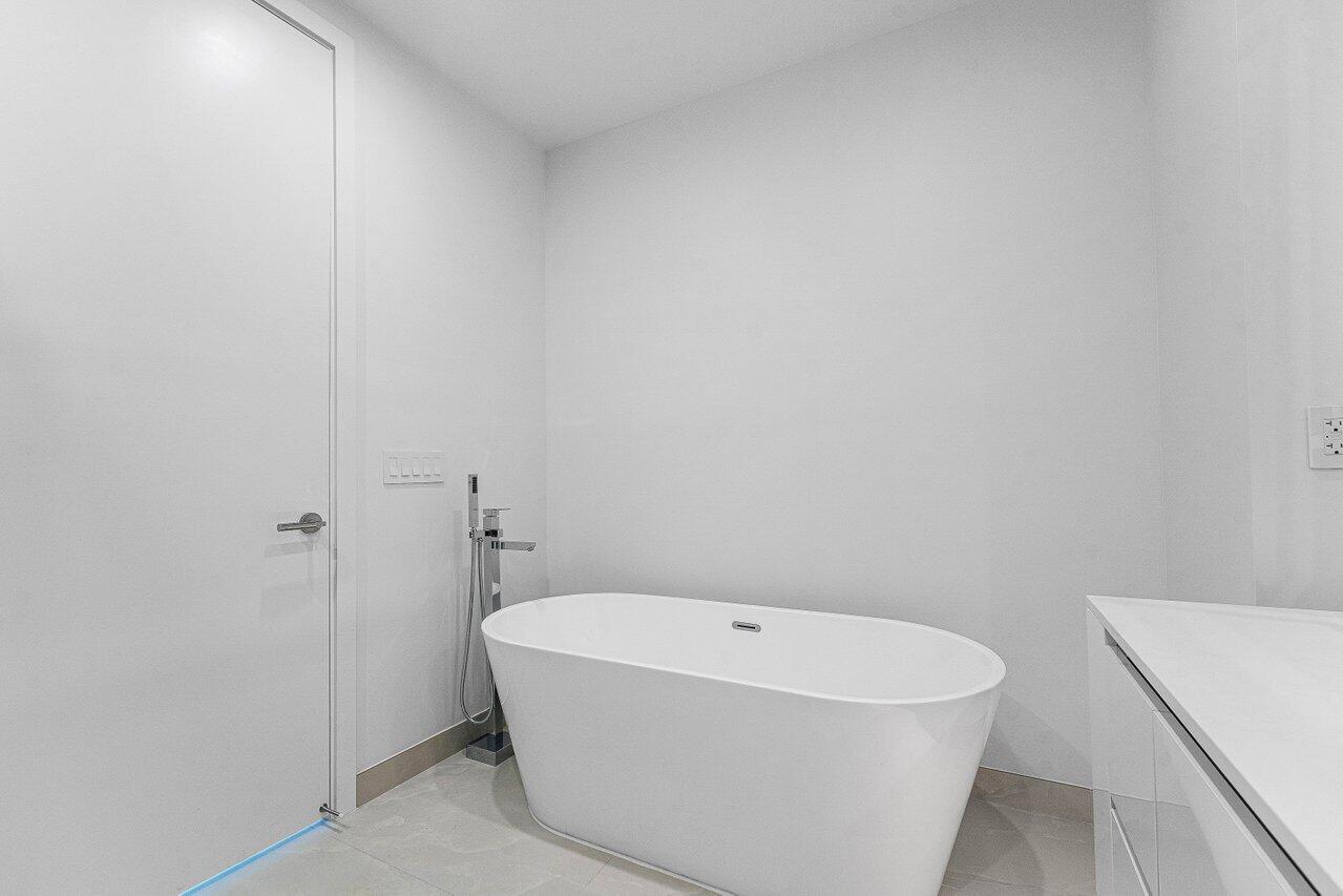 Freestanding white soaking tub with a floor-mounted chrome faucet and handheld sprayer, set against polished tile flooring
