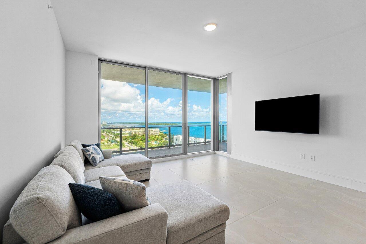 Floor-to-ceiling sliding glass doors, ceramic tile flooring, and a glass-paneled balcony featuring coastal and urban scenery