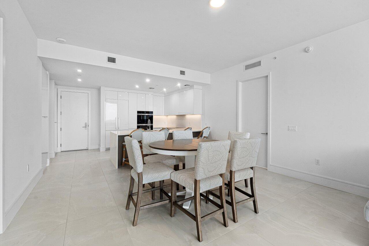 Open-concept kitchen featuring high-gloss white cabinetry, a center island with integrated seating, recessed lighting, and large-format tile flooring