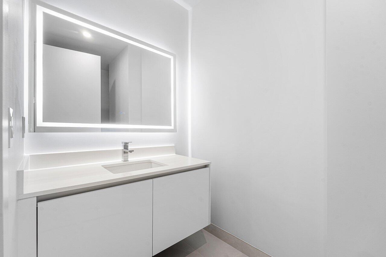 Floating vanity featuring flat-panel cabinetry, a light-toned countertop with an integrated sink, polished chrome faucet, and a large rectangular LED-backlit mirror