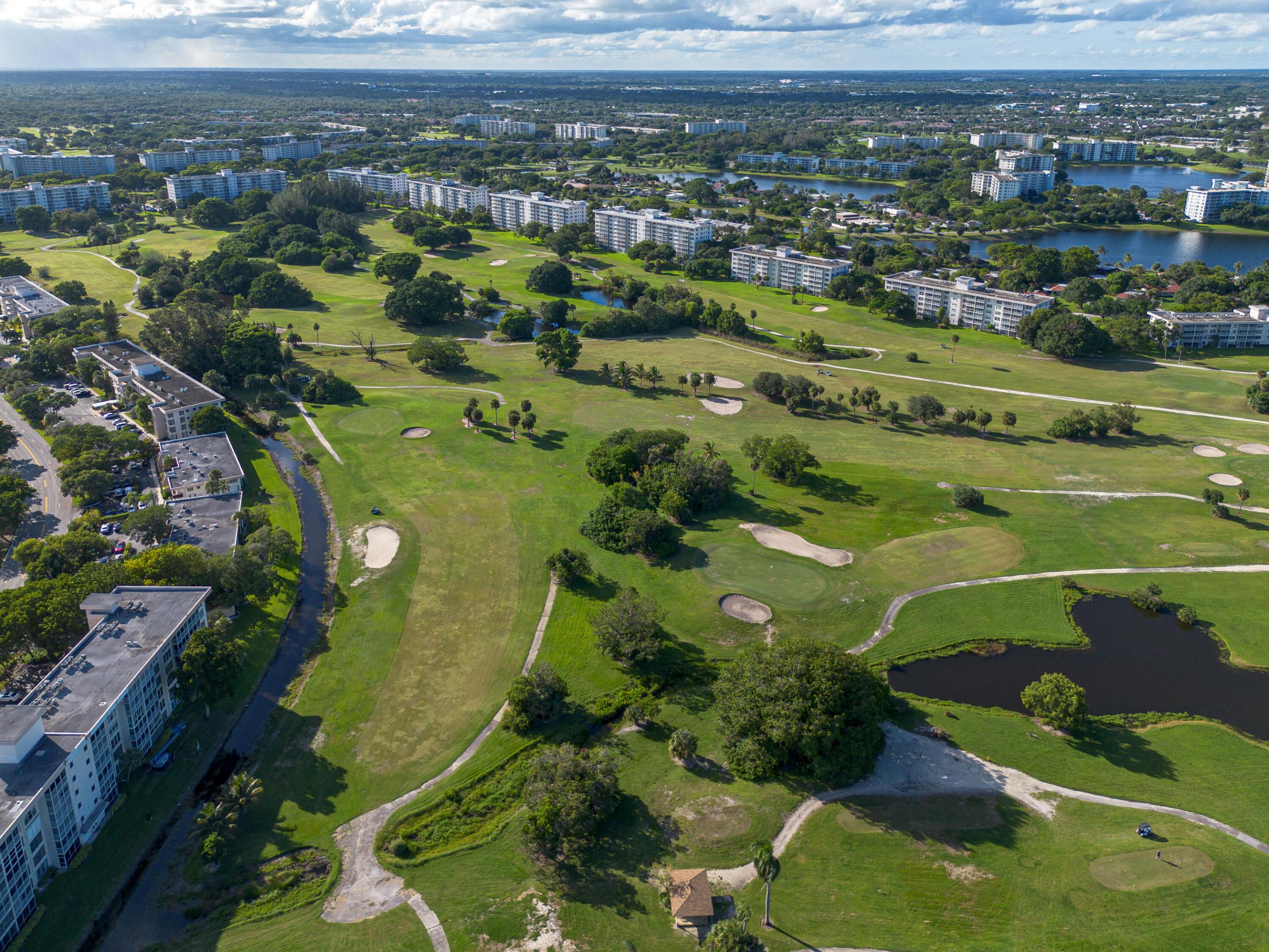 Aerial perspective featuring expansive golf course grounds, sand bunkers, manicured green spaces, mature trees, and water features