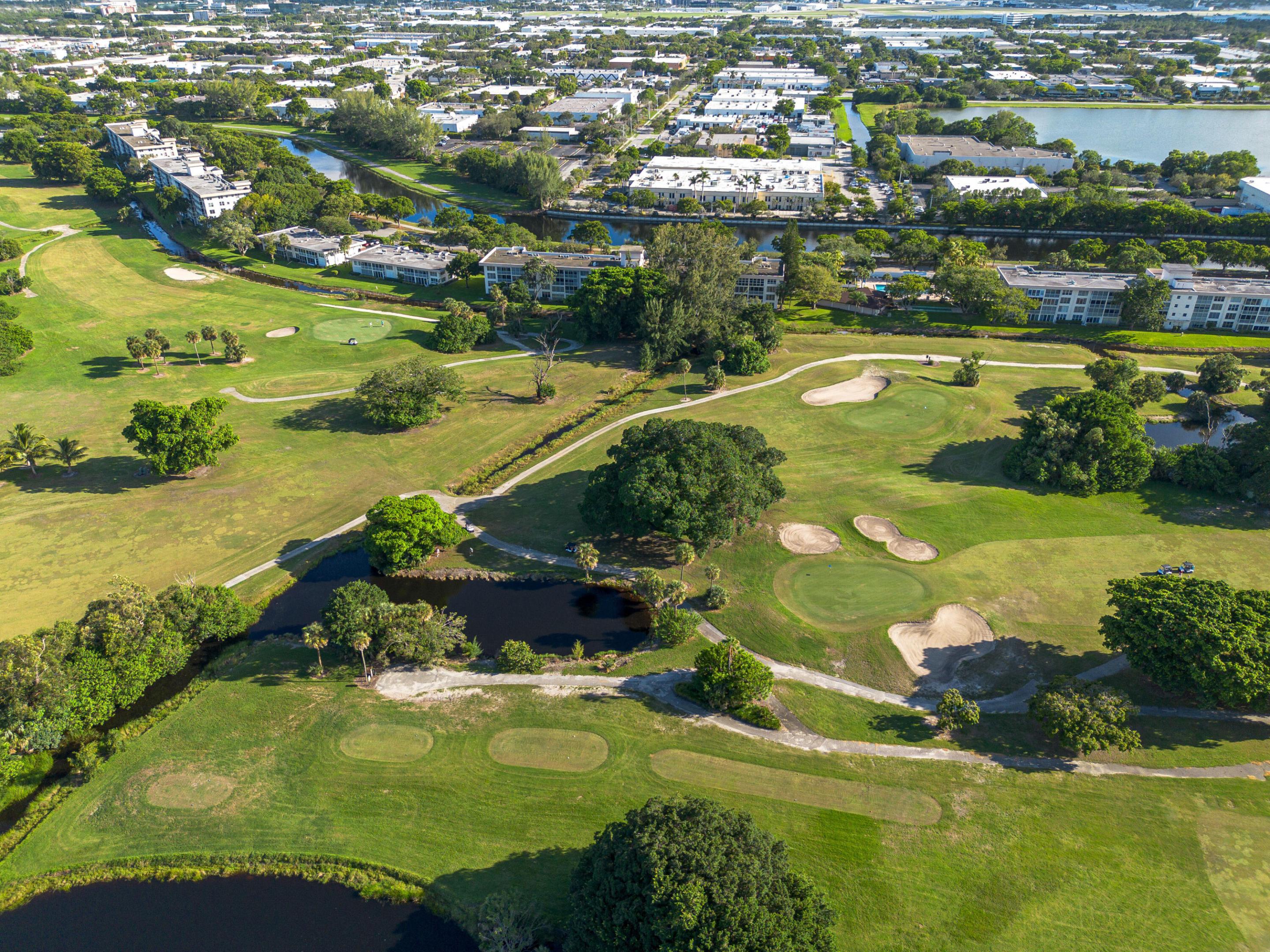 Aerial perspective of a golf course featuring expansive green fairways, sand bunkers, mature trees, and water features