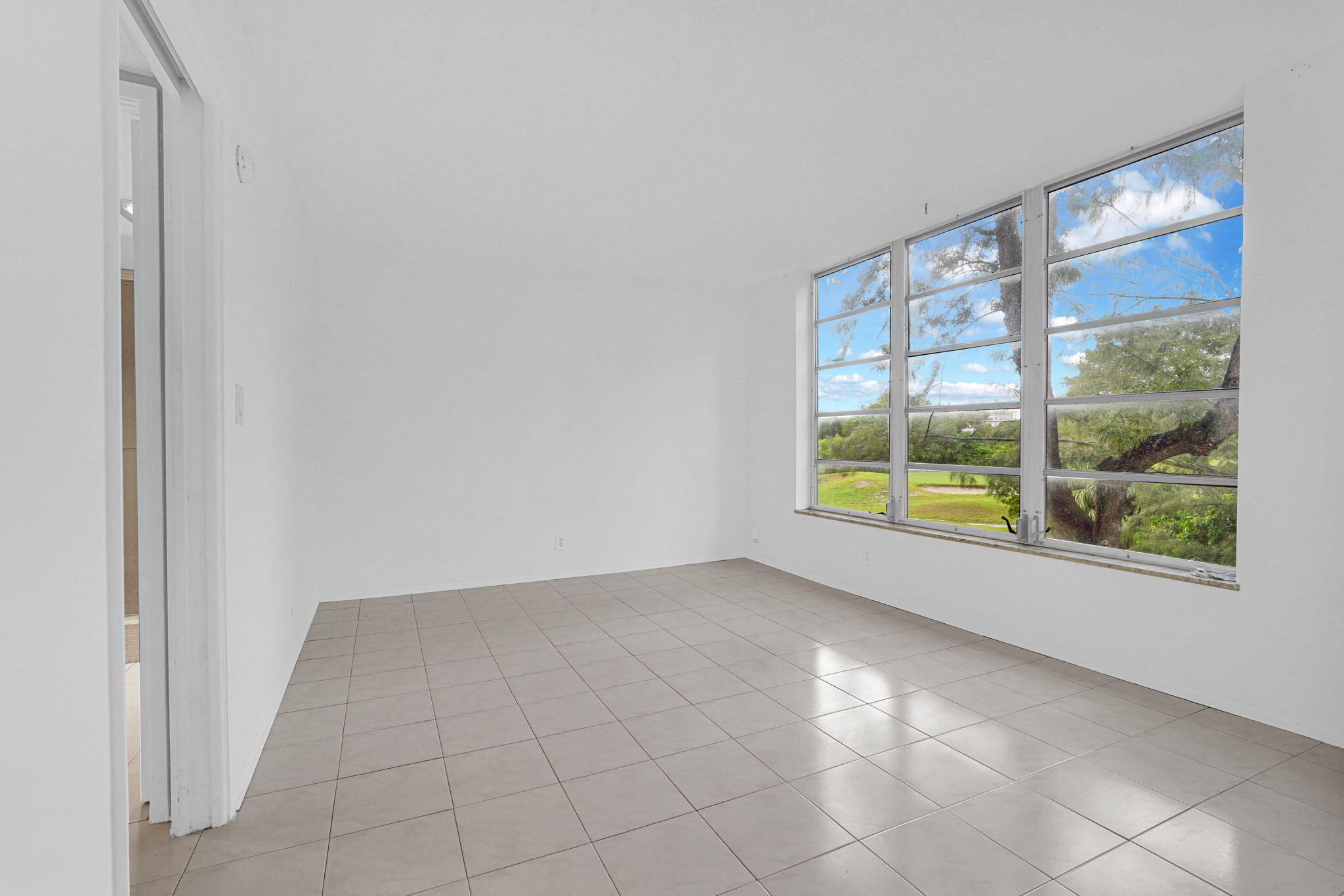 Interior space featuring large-format tile flooring, crisp white wall finishes, and a expansive multi-pane window configuration showcasing outdoor greenery